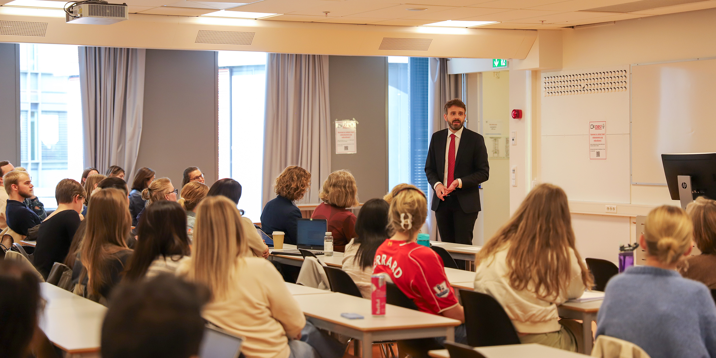 Foto av helseminister Vestre som står foran studenter i et klasserom og foreleser.