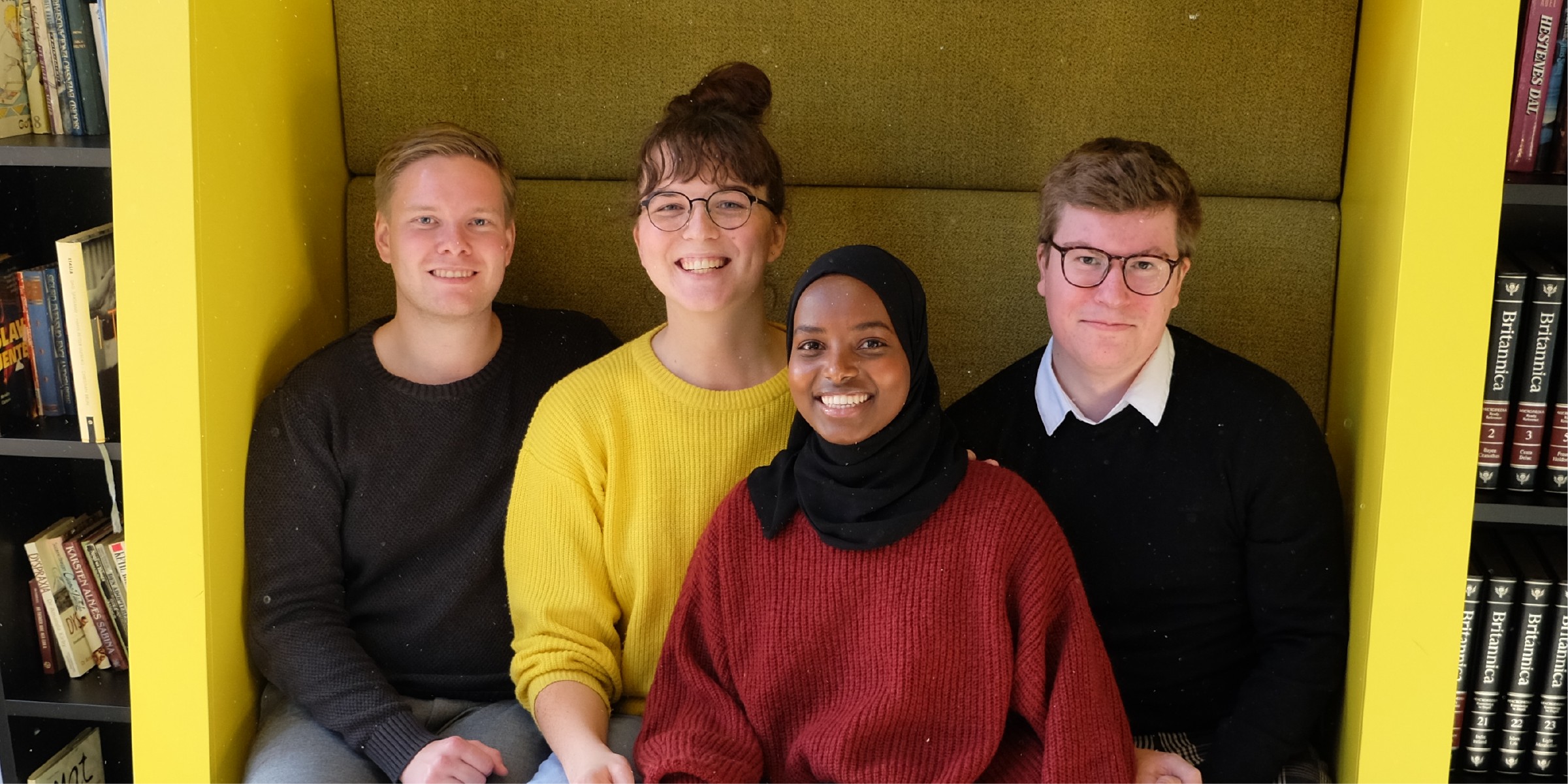 De fire medlemmene i Arbeidsutvalget i Studentparlamentet sitter i en gul sofa og smiler til kamera.