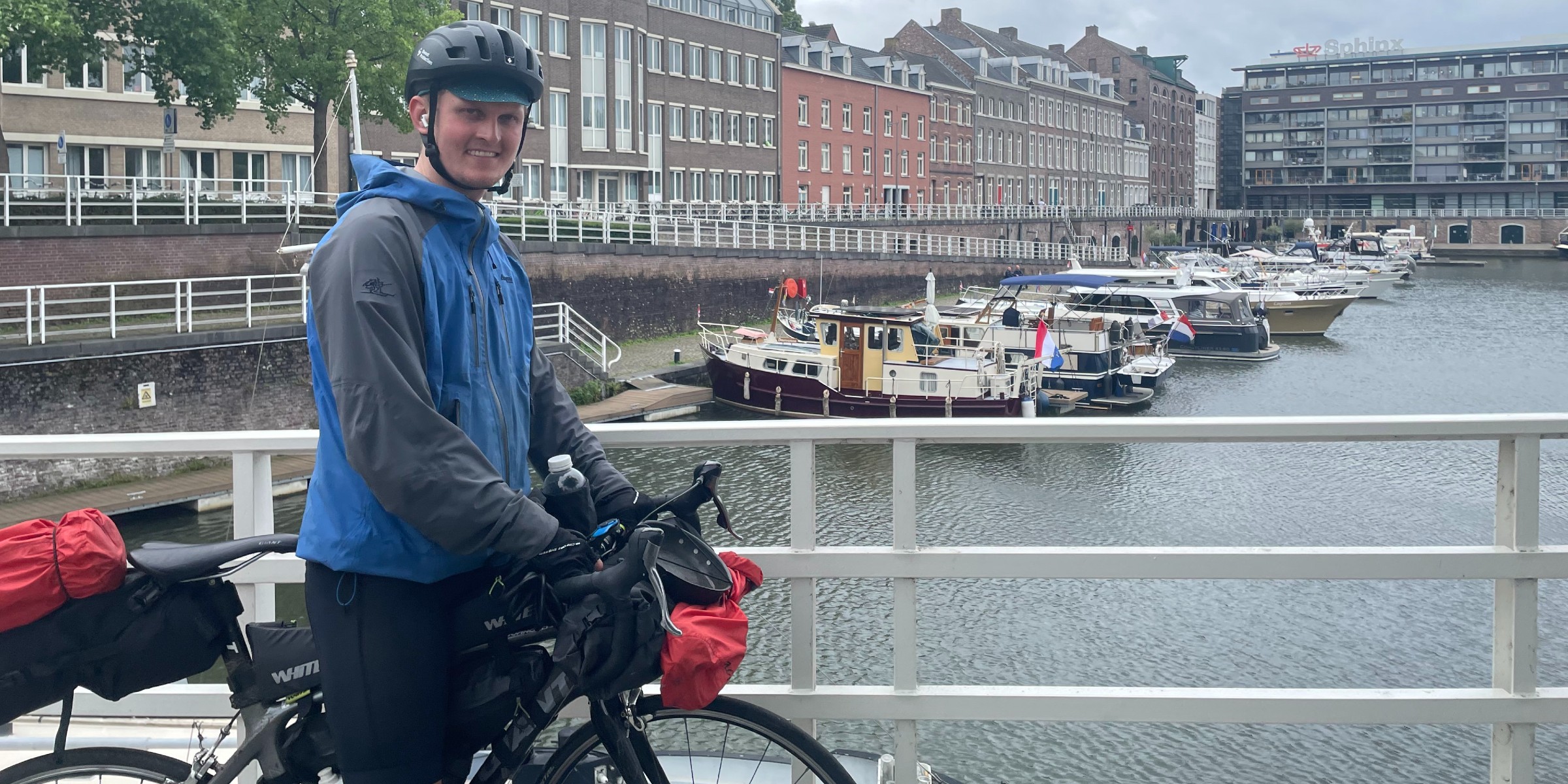 OsloMet-student Åsmund is standing with his bike on a bridge over a river in Maastricht in the Netherlands. He is smiling at the camera.