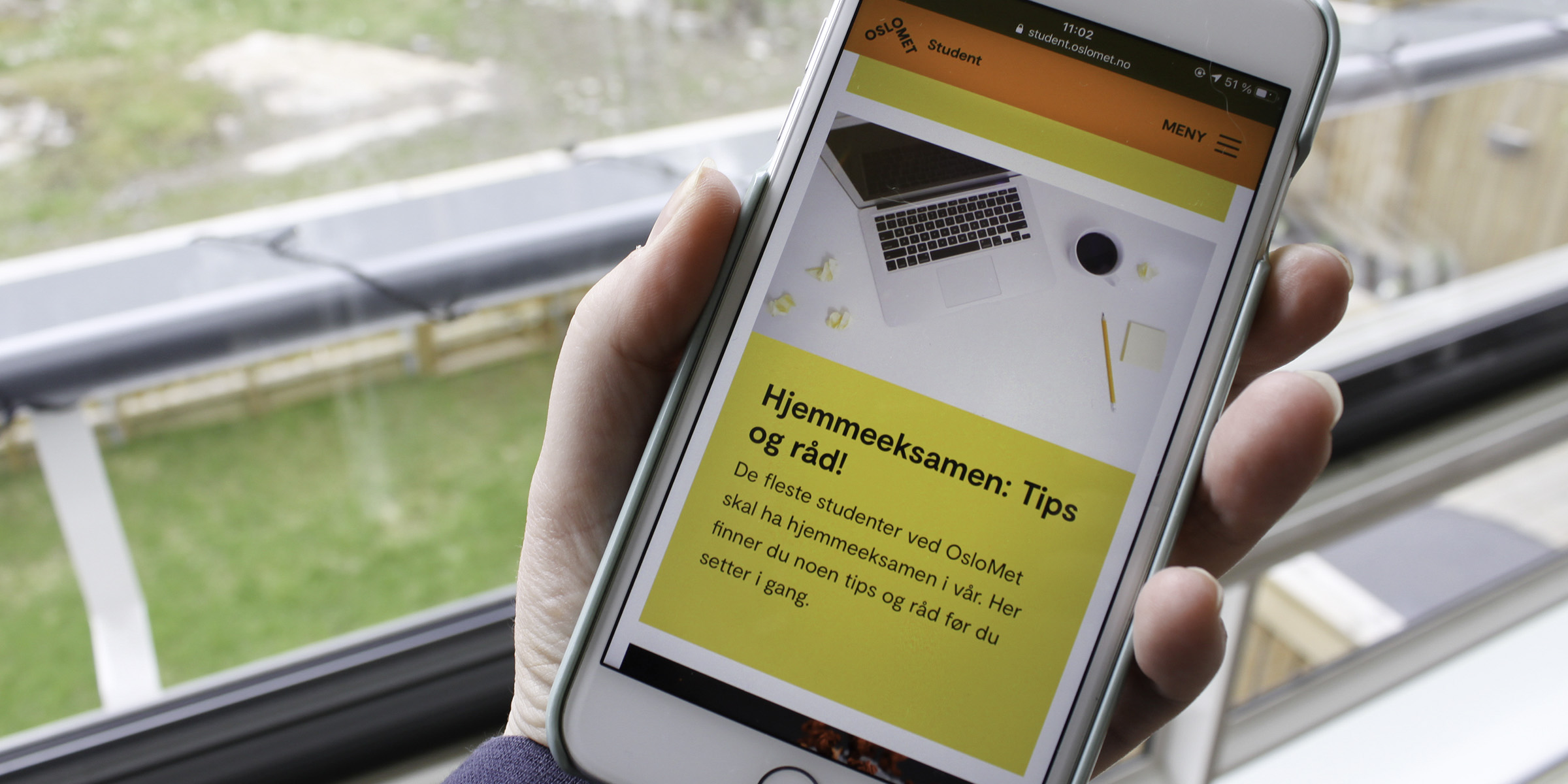 Noen holder i en mobiltelefon og viser frem nettsiden student.oslomet.no på mobilens skjerm.