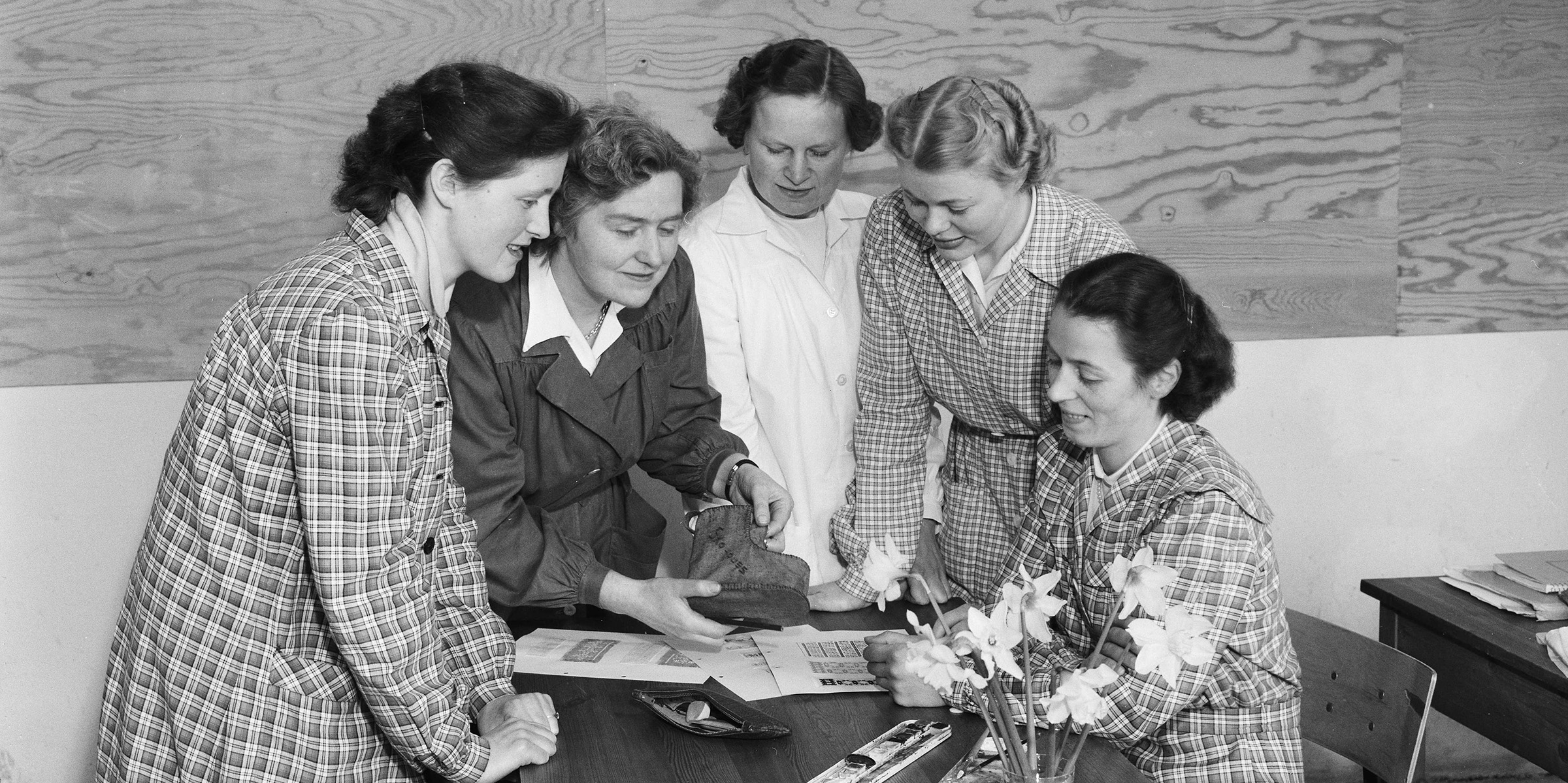 Studenter ved Statens kvinnelige industriskole sitter rundt et bord og ser på noen arbeider.