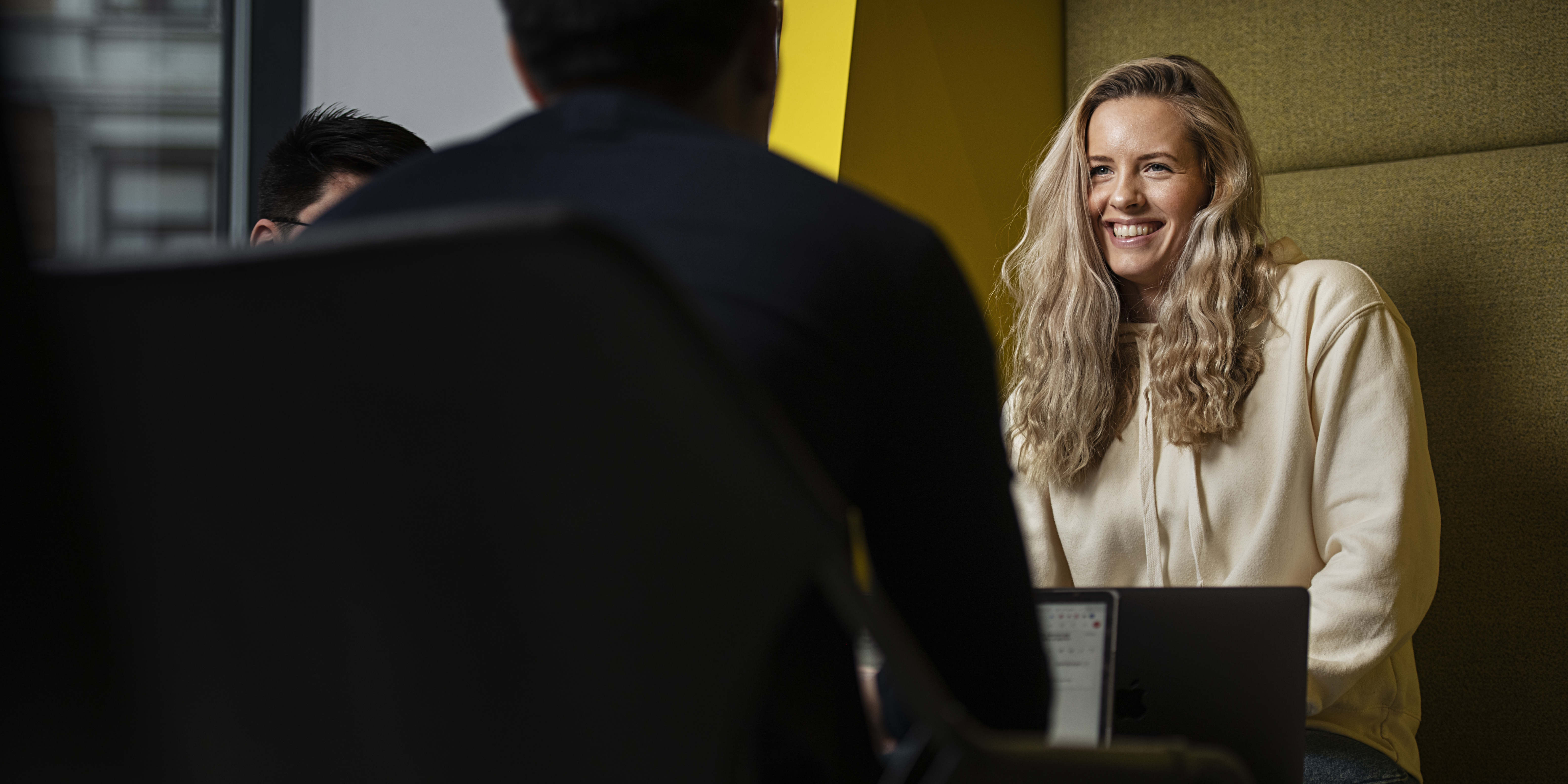 Dame som sitter i en sofa og smiler.