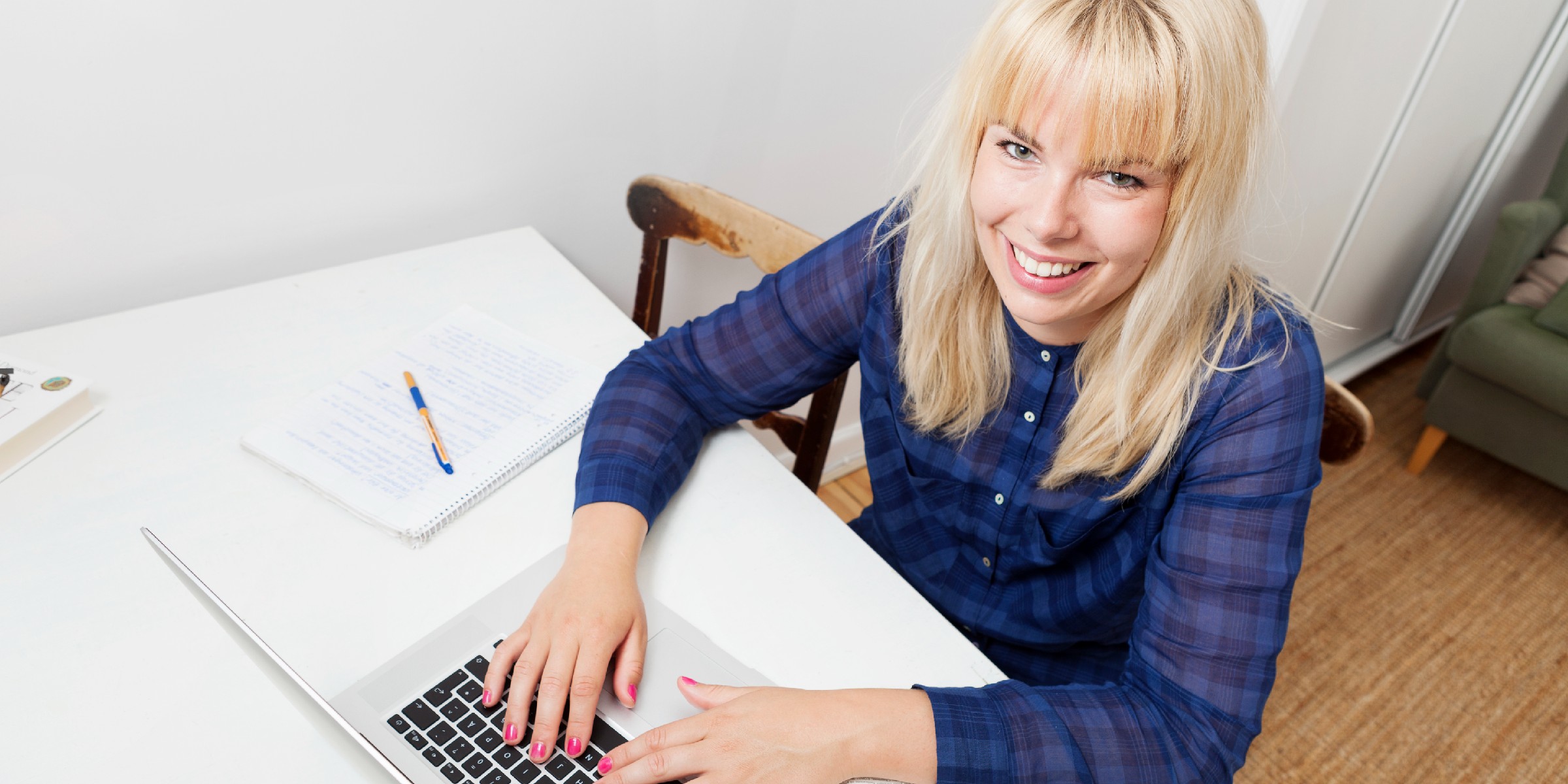 Student sitter foran laptop, ser opp mot kamera og smiler.