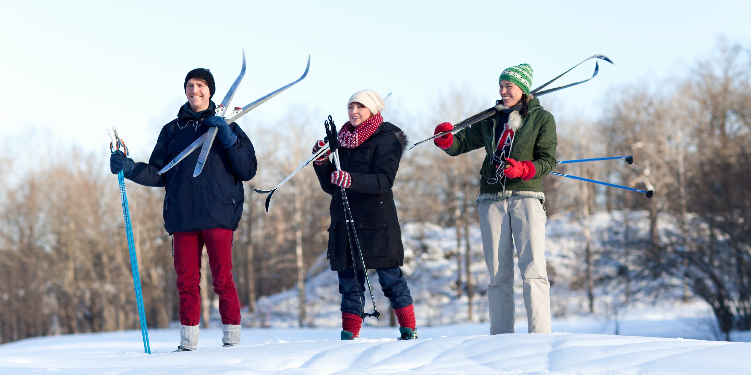Three young adults hold cross-country skis over their shoulders and look out over the landscape while smiling.