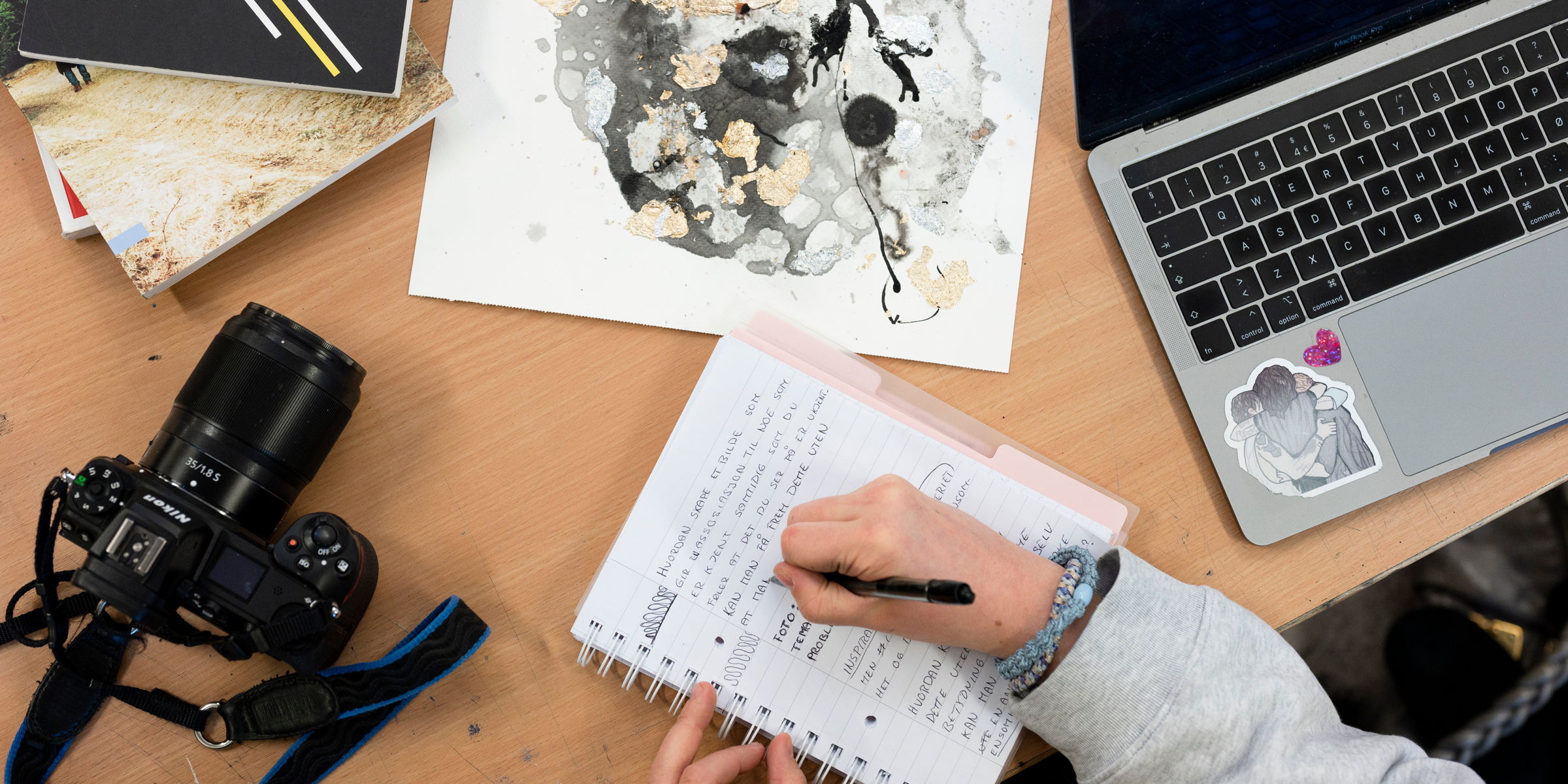 Sett ovenfra, kamera, en tegning og en PC. Samt en notatbok, som noen skriver i.
