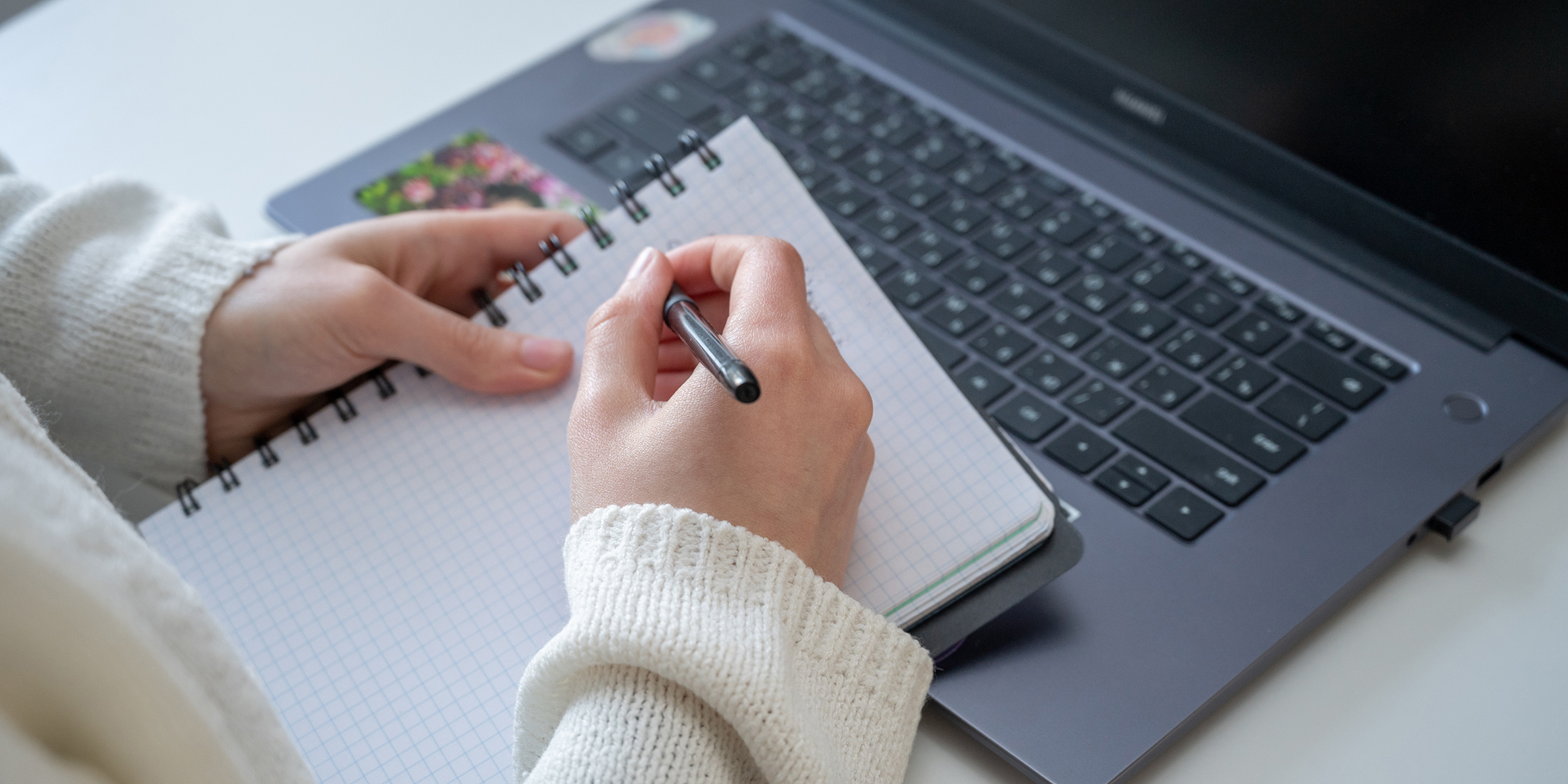 Student skriver på notatblokk over datamaskin.