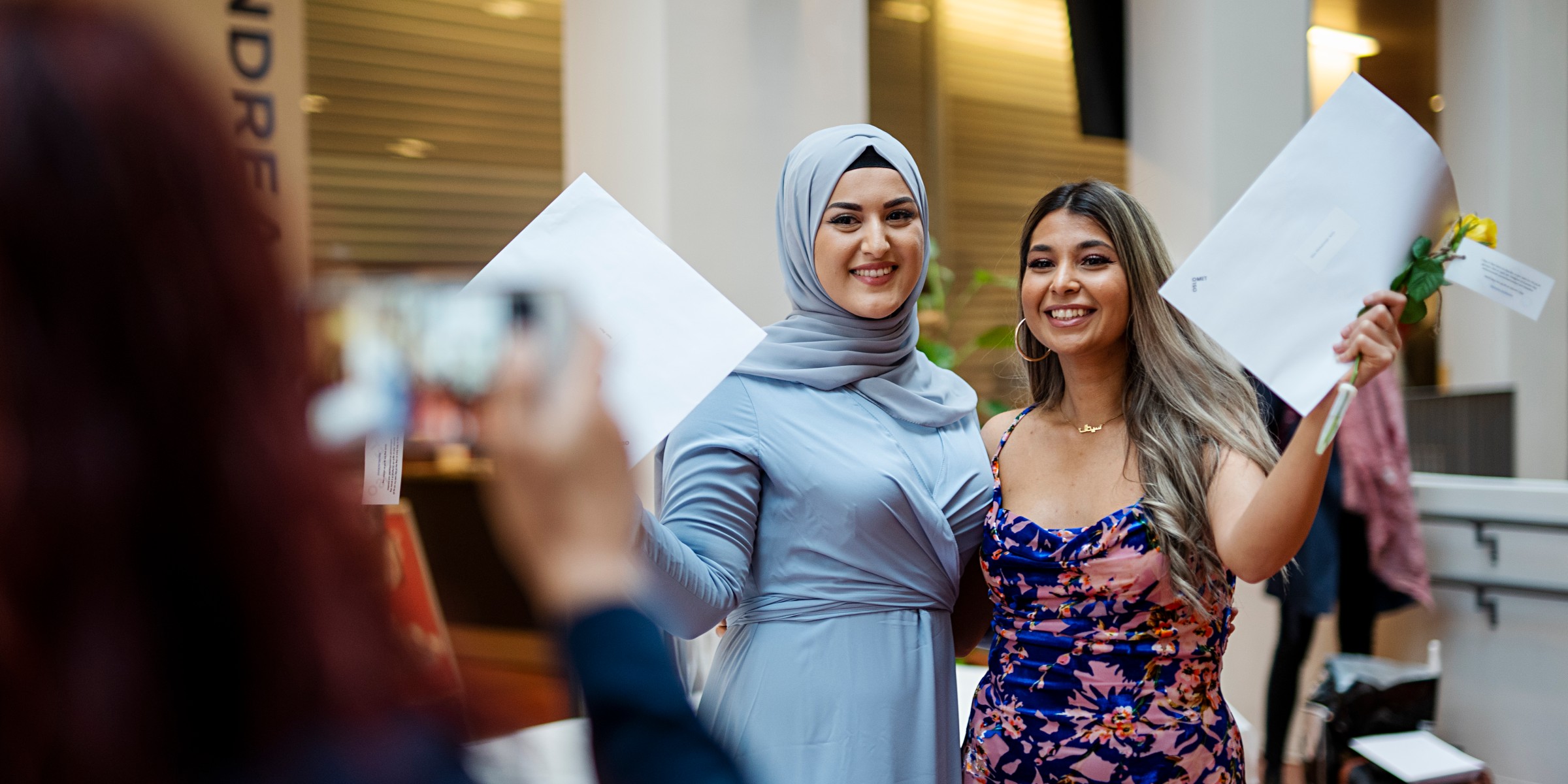 To kvinnelige avgangsstudenter smiler mot fotografen.