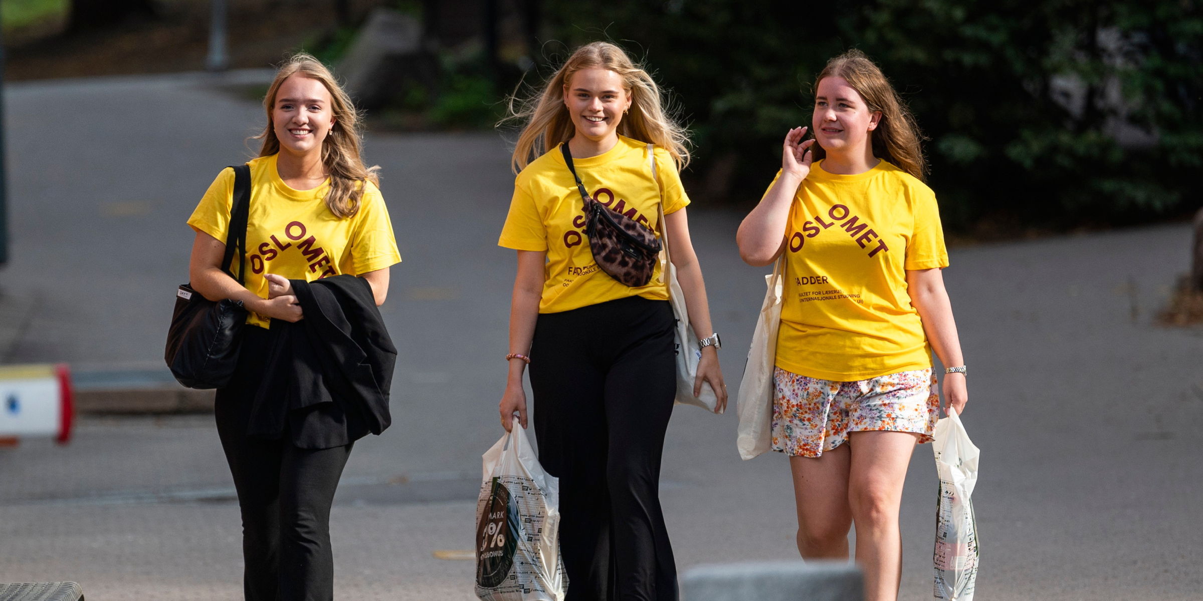 Tre OsloMet-studenter i gule t-skjorter kommer gående mens de smiler.