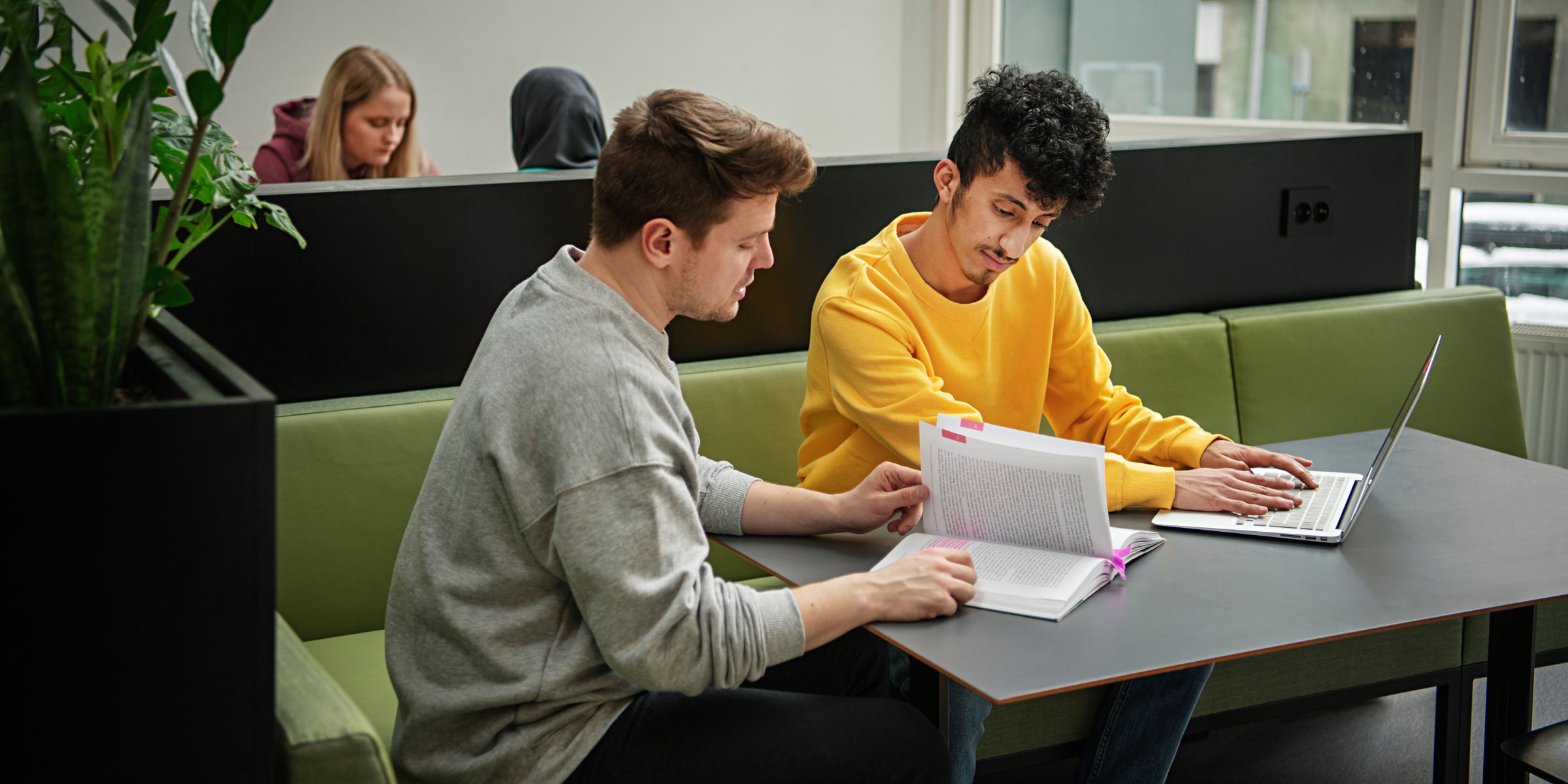 To OsloMet-studenter sitter i en sofagruppe. Begge ser i ei bok og en av dem har hendene på laptoptastaturet.
