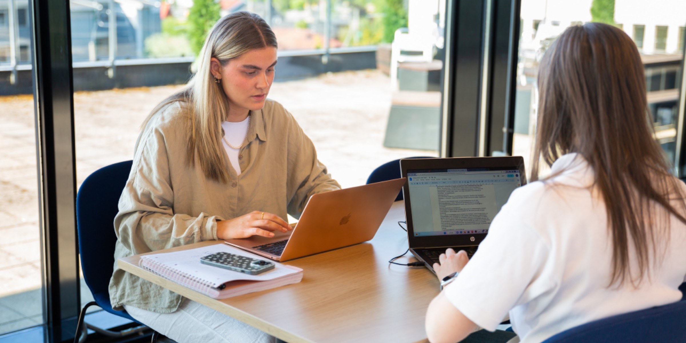 To studenter sitter på et bord og jobber på pc.