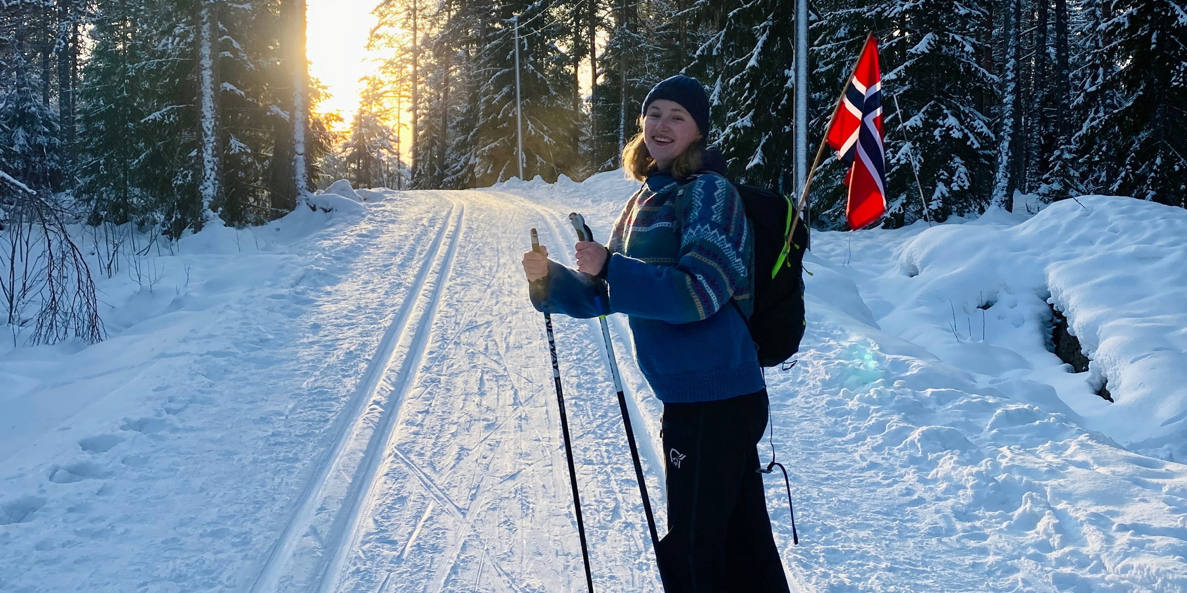 OsloMet-student ute på ski. Et norsk flagg stikker opp av ryggsekken hennes og hun smiler til kamera.