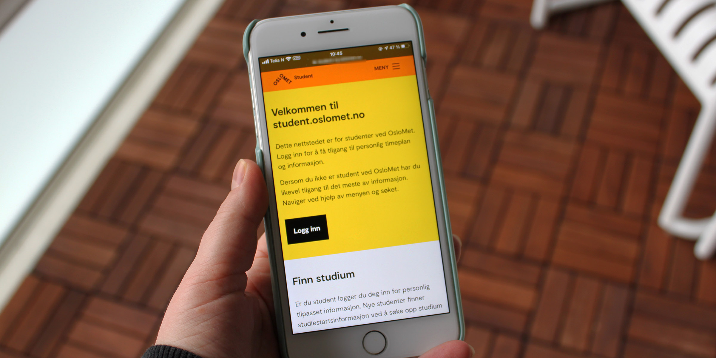 Hånd som holder iPhone med bilde av fremsiden til studentnettsidene.