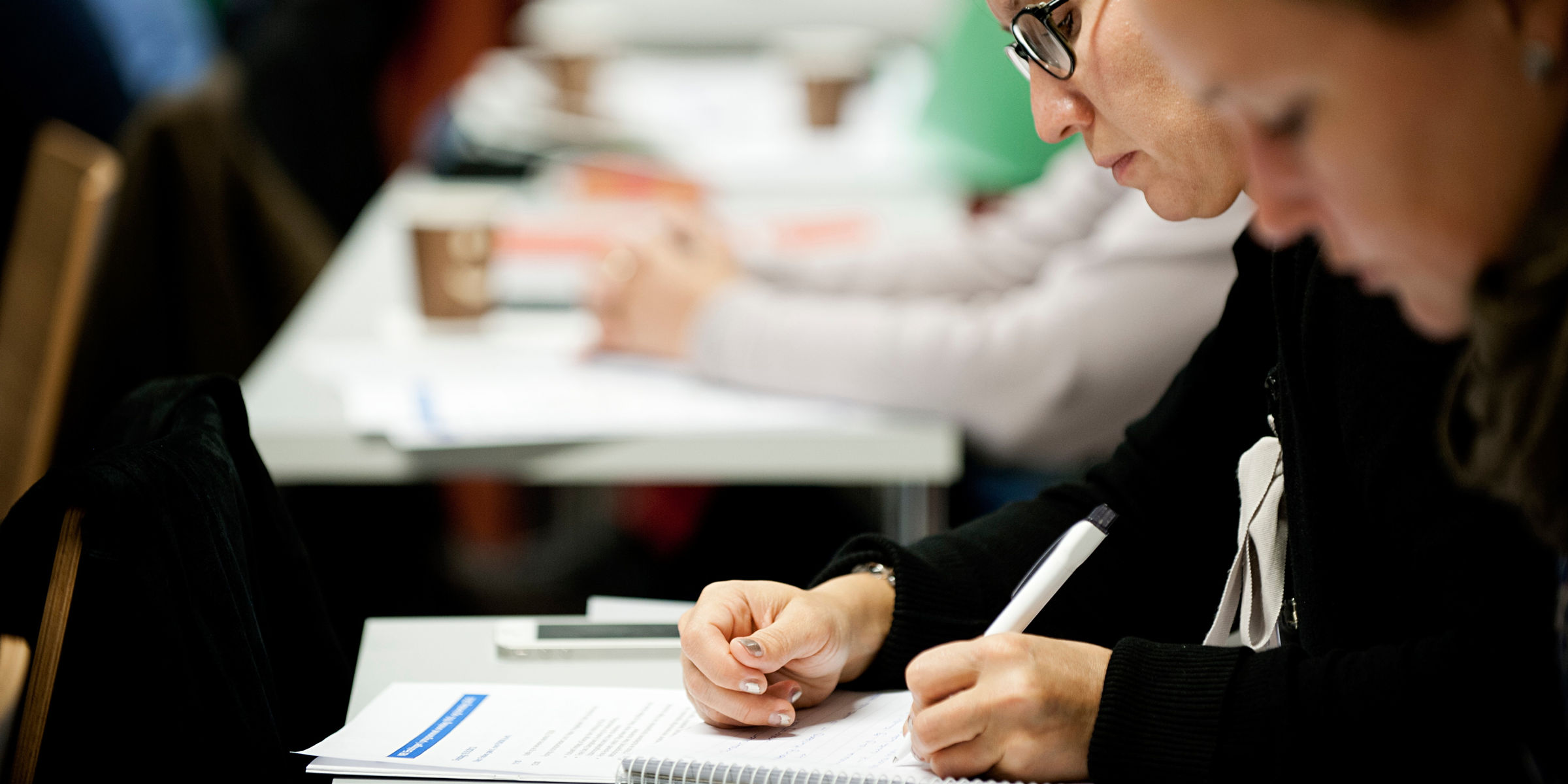 Two students have a written exam together with other students.