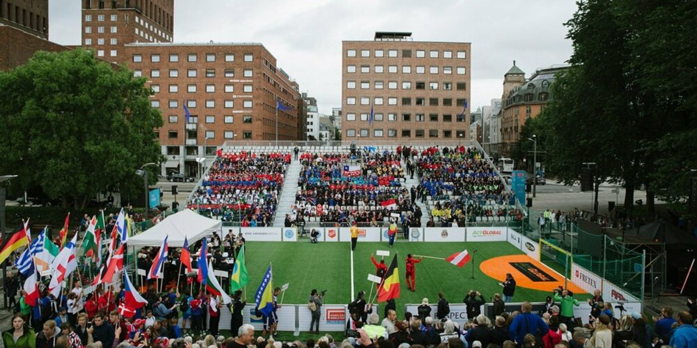 A football field surrounded by people with flags from different parts of the world and a grandstand full of spectators outside the City Hall in Oslo.