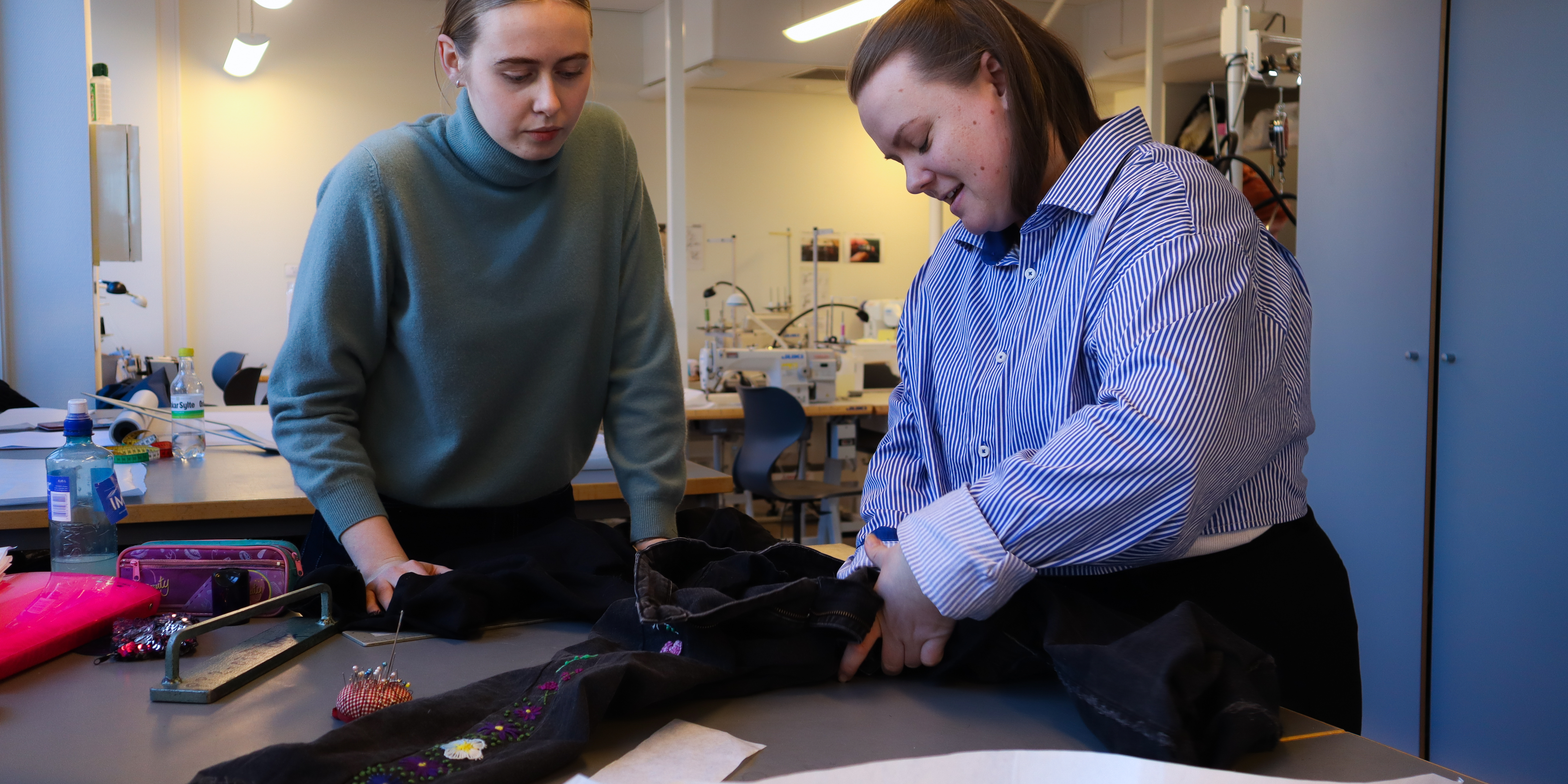 Kunst- og designstudentene Emilie og Anne reparerer en bukse i et klasserom på OsloMet.