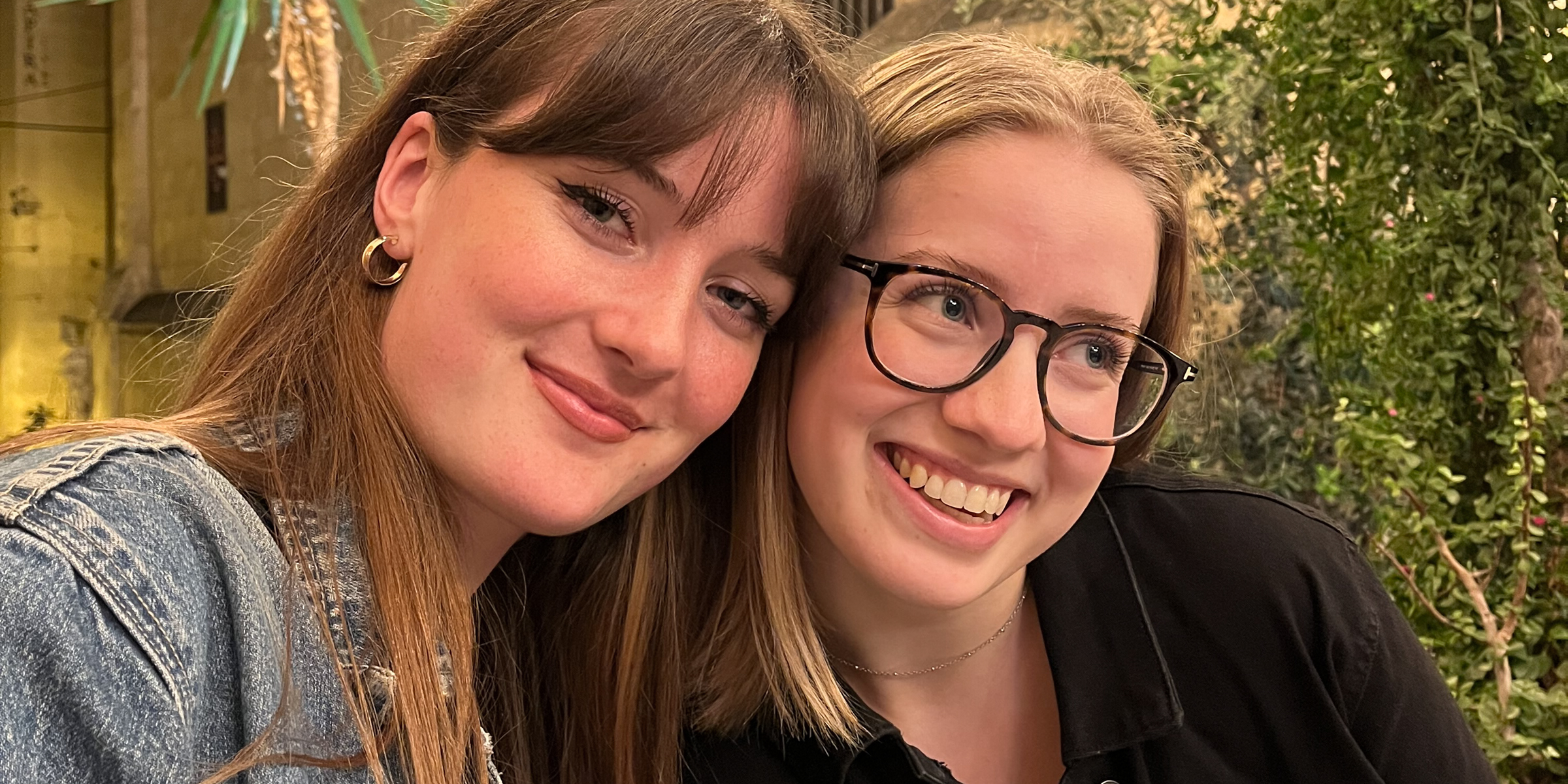 Sykepleiestudentene Sara og Dina sitter tett sammen. Begge smiler.