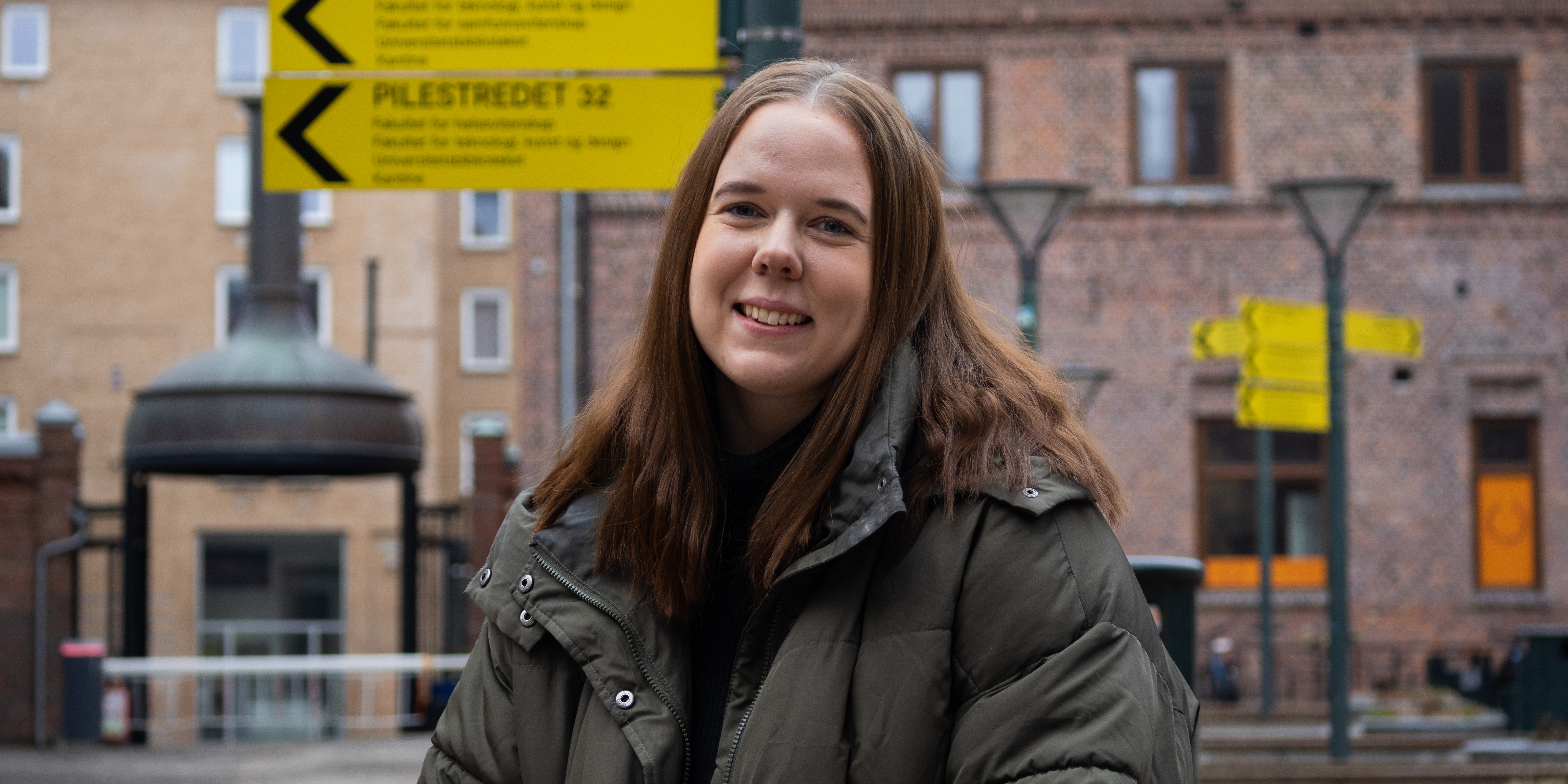 OsloMet student stands outside on campus and smiles at the camera.