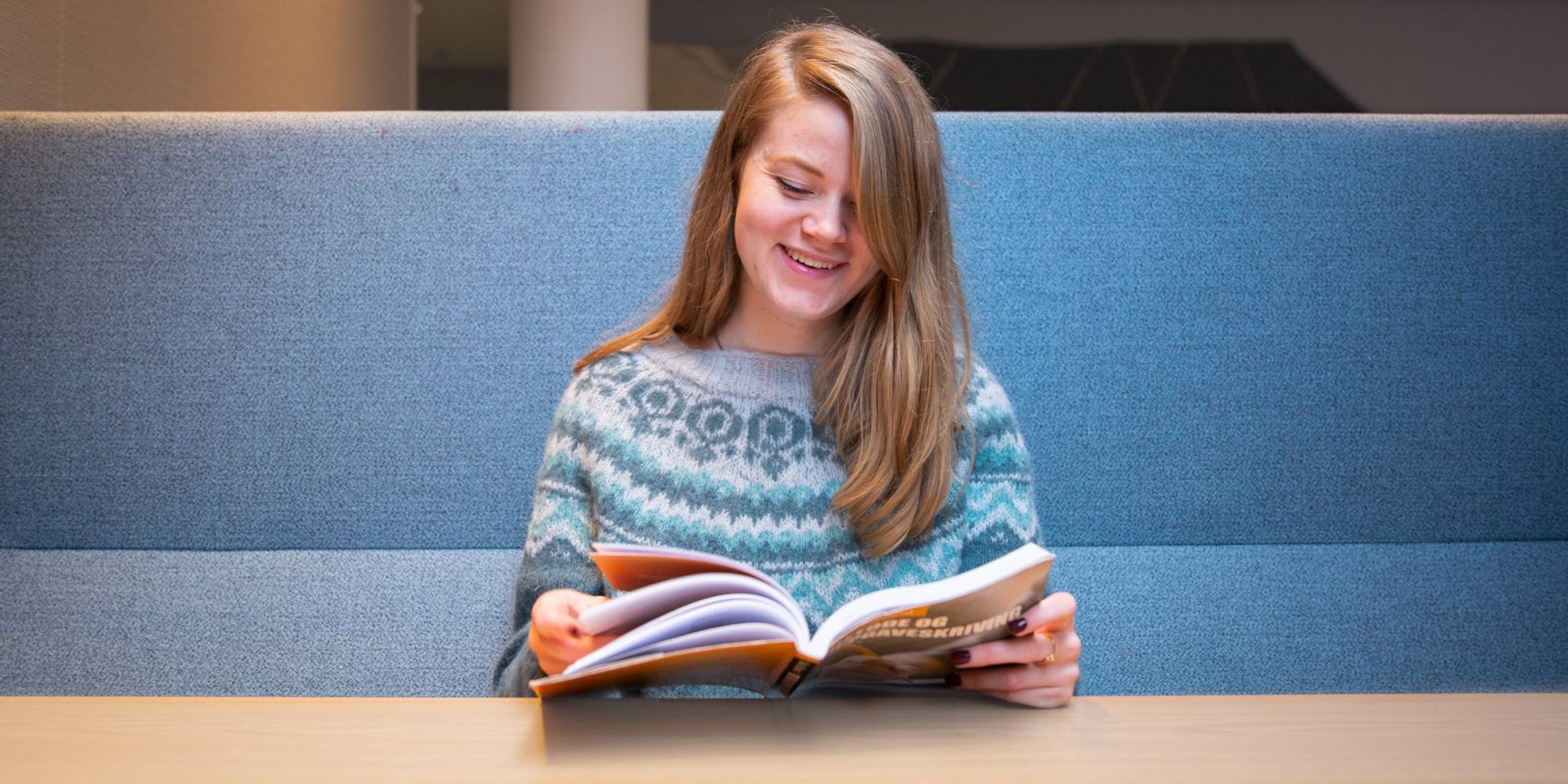 OsloMet-student som sitter og leser i en pensumbok mens hun smiler.