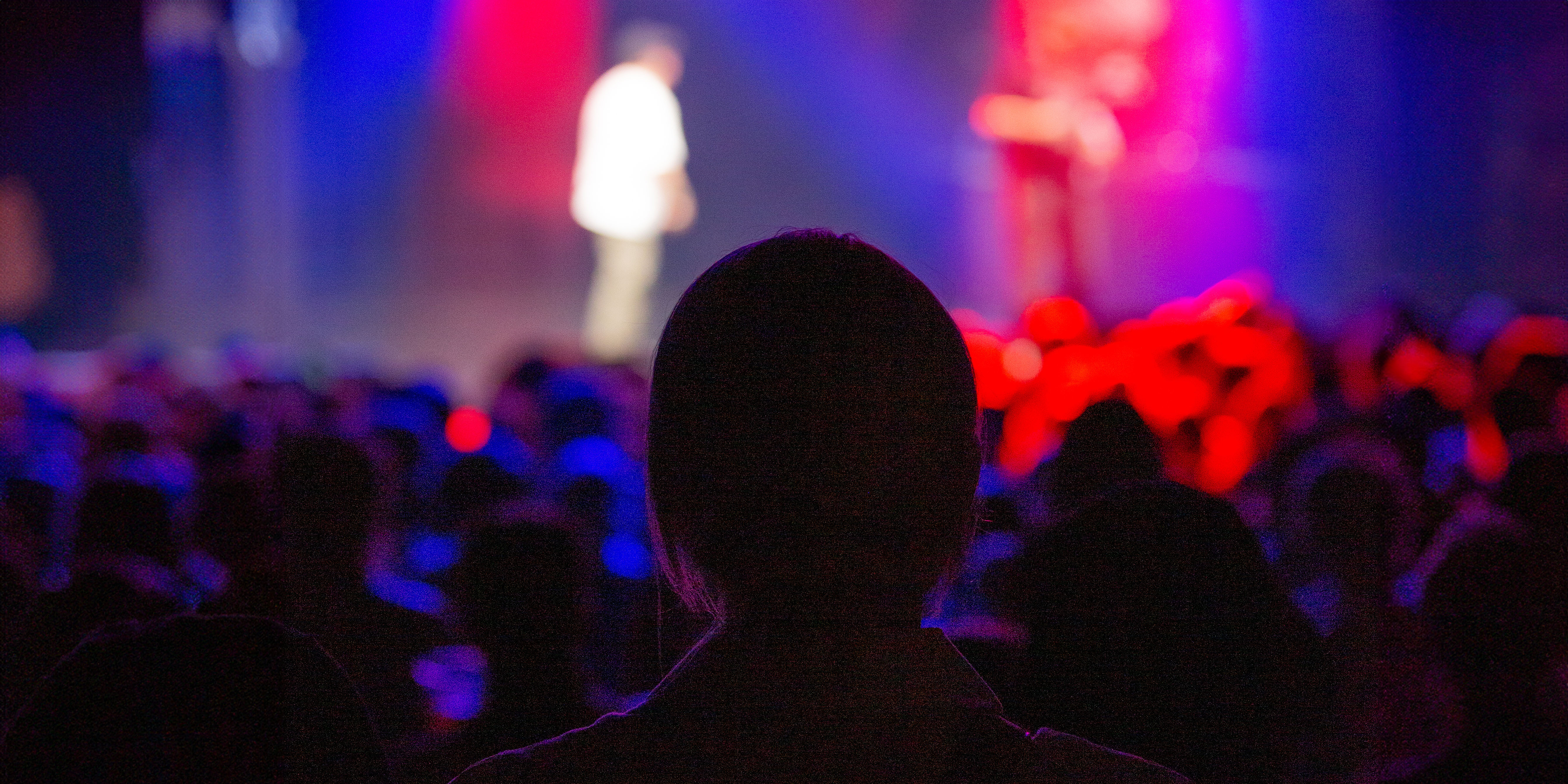 Publikum ser på scenen i et mørkt konsertlokale.