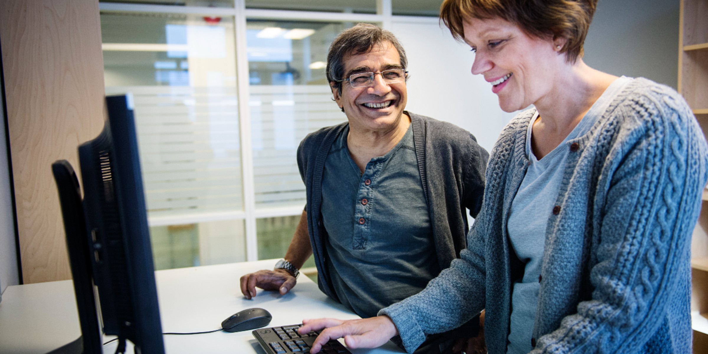 Image of two people standing in front of a computer.