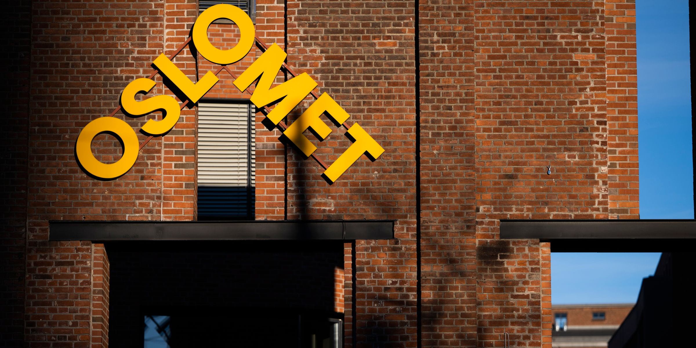 Yellow OsloMet-logo on a brick wall.
